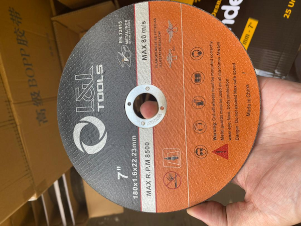 Disco de corte L&L Tools 7 pulgadas 180x1.6x22.23mm sostenido en mano con cajas de inventario al fondo